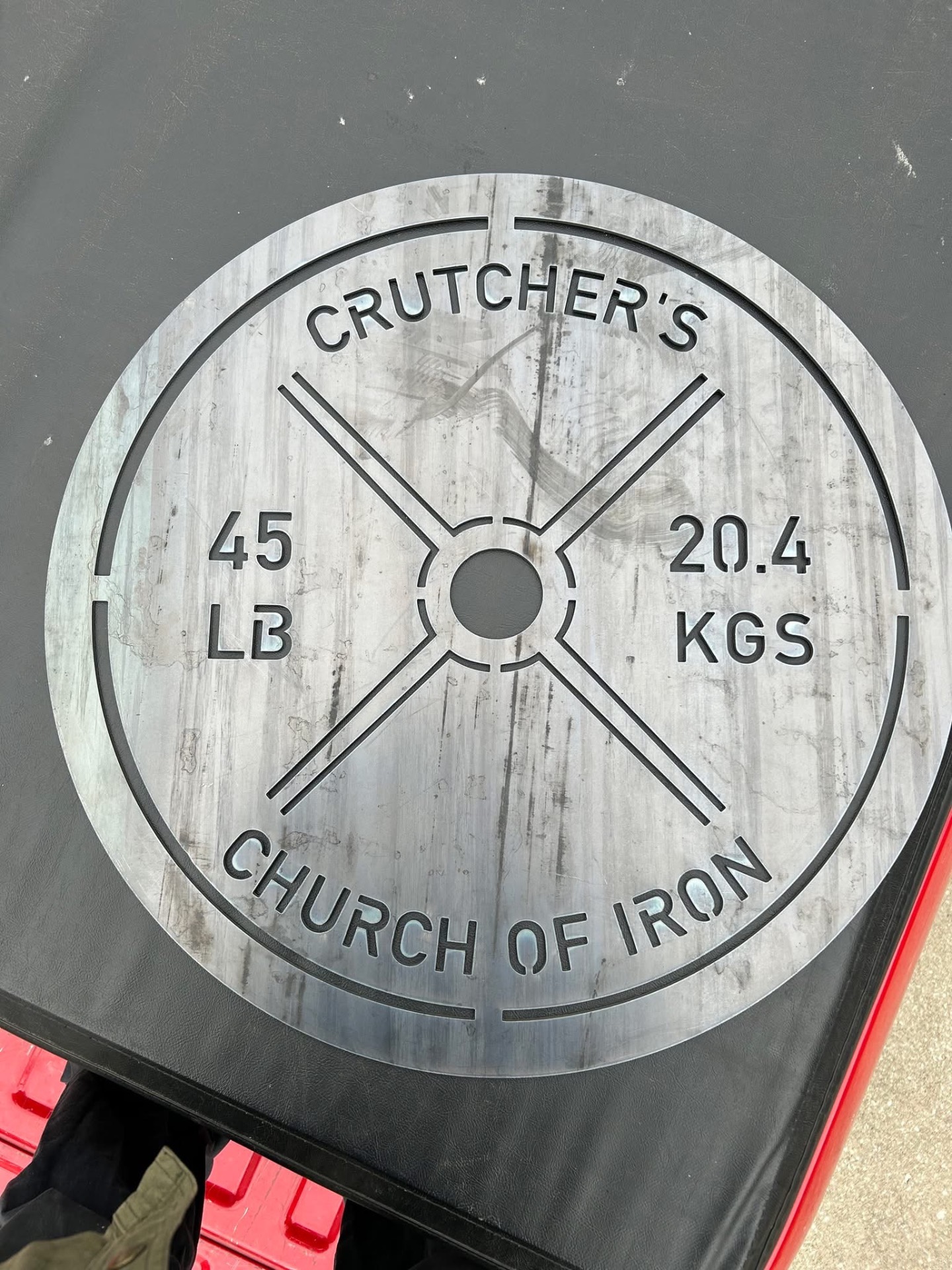 Plasma-cut steel weight plate sign reading 'Crutcher's Church of Iron 45 LB / 20.4 KGS'