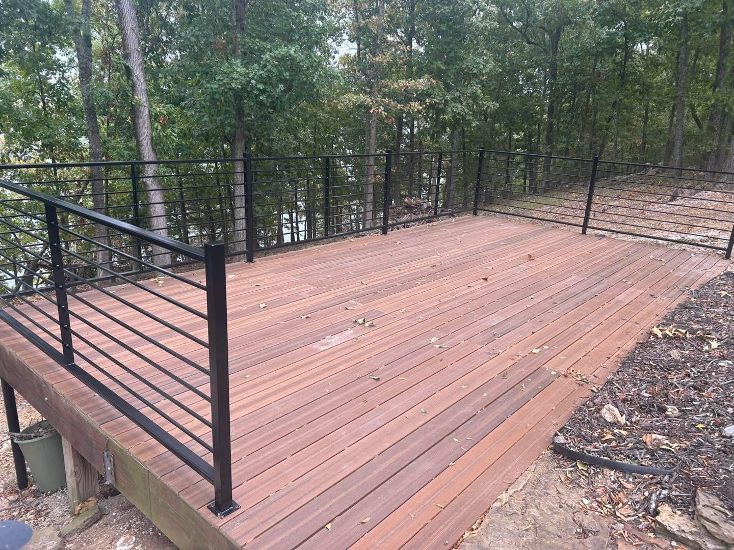 Composite deck wrapped with custom black horizontal metal railing in the woods